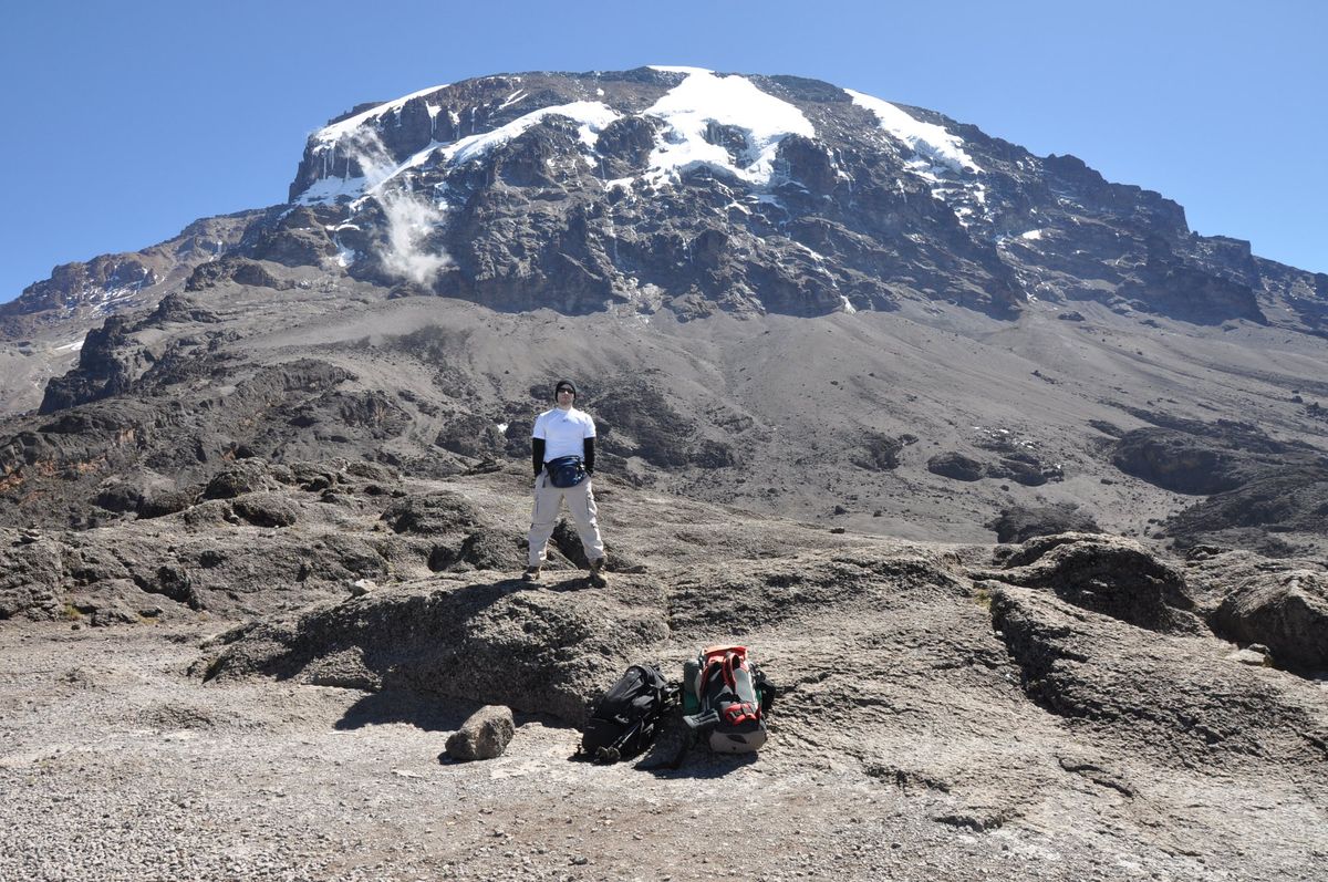 A trekker on rocky ground with the snow-capped summit of Kilimanjaro behind