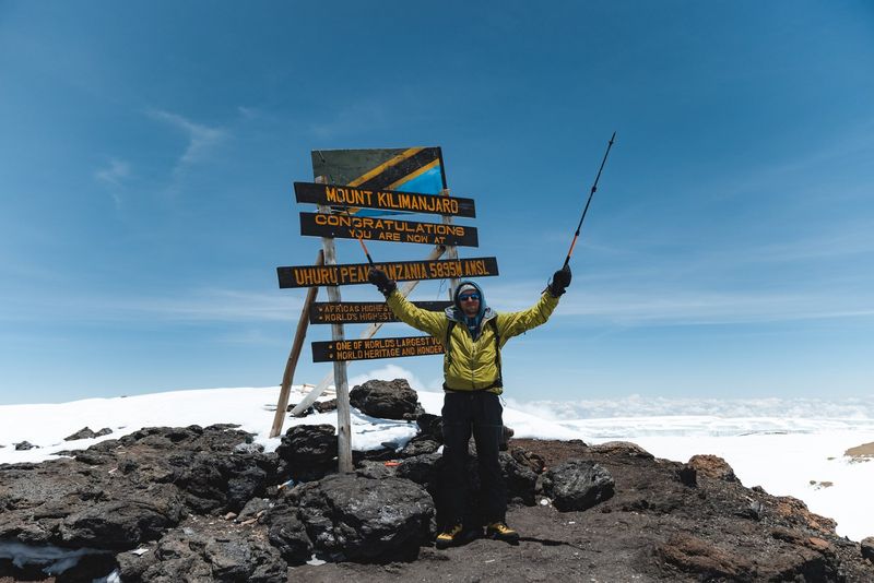 A climber celebrating beside the summit sign at Uhuru Peak